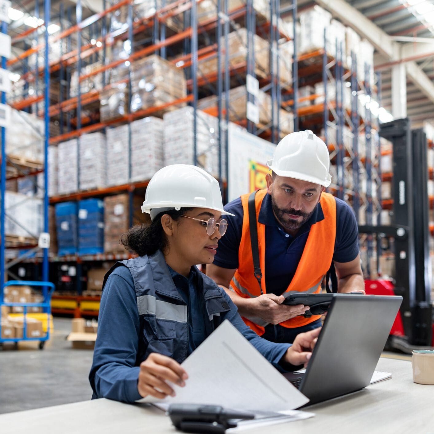 Inspector talking to an employee and using a laptop at a warehouse